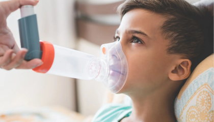 Child Laying back on a cushion with an adult placing an asthma puffer and spacer on the child