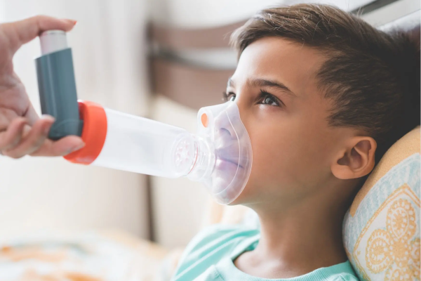 Child Laying back on a cushion with an adult placing an asthma puffer and spacer on the child