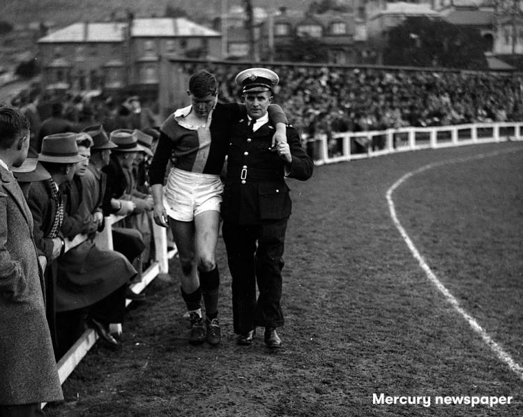 A picutre from the 50's of a st john volunteer helping a patient on a sports ground